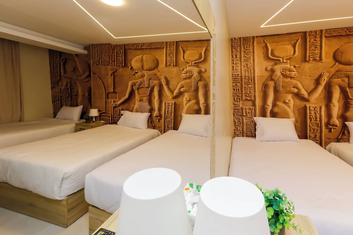 Et hotelværelse med to senge, en væg med egyptiske udskæringer, og et natbord med en lampe.