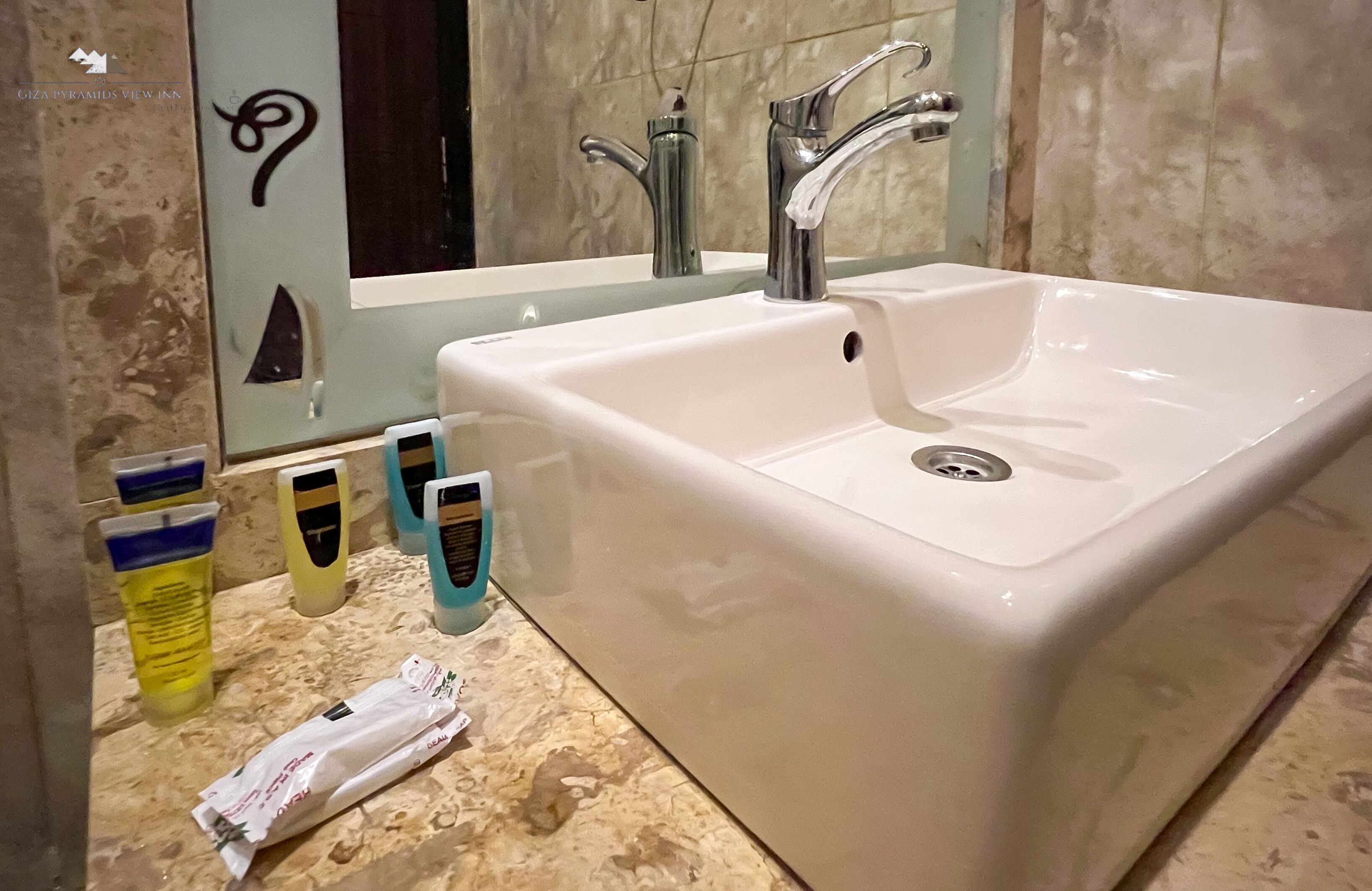 A bathroom with a large white sink, two faucets, and a mirror above it. There are toiletries on the counter.
