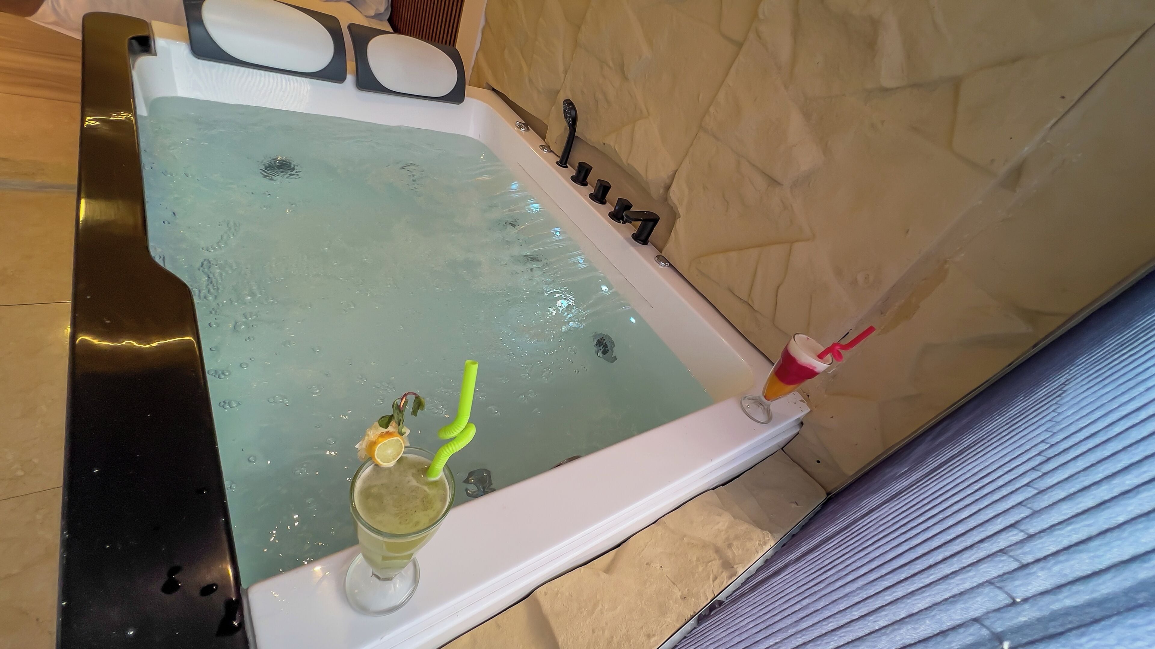 A bathtub with a glass of drink and a green straw, a bottle of shampoo, and a bottle of lotion.