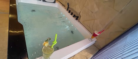 A bathtub with a glass of drink and a green straw, a bottle of shampoo, and a bottle of lotion.