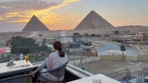 A person seated at a table with a view of the pyramids and a desert landscape.