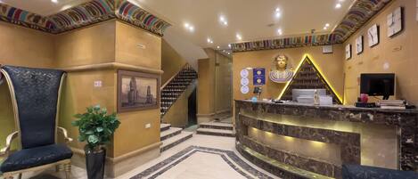 A reception area with a marble reception desk, a large chair, a potted plant, and a staircase leading to upper floors.