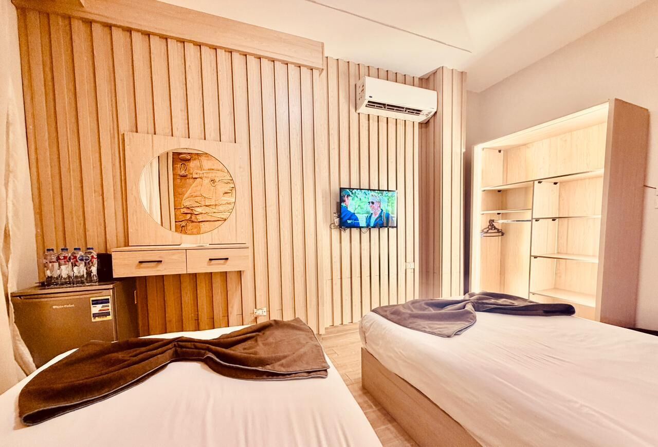 A hotel room with two beds, a wooden wall paneling, a television, a minibar, and a wardrobe.