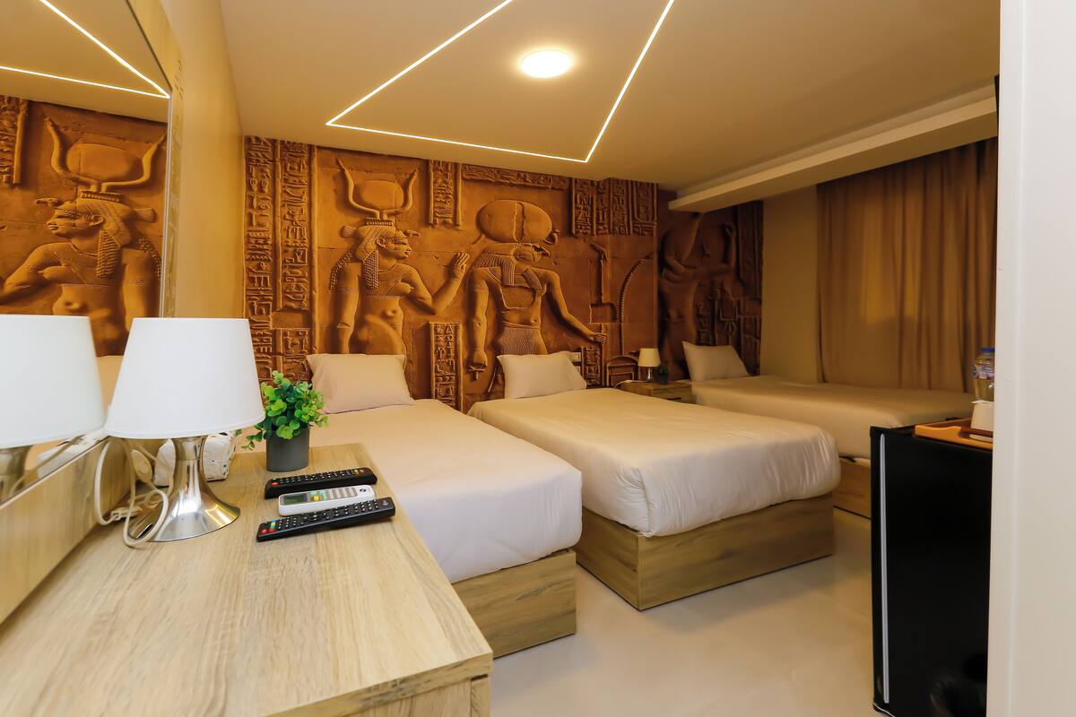 Et hotelværelse med to senge, et skrivebord med lampe, et fjernsyn og egyptiske vægudskæringer.