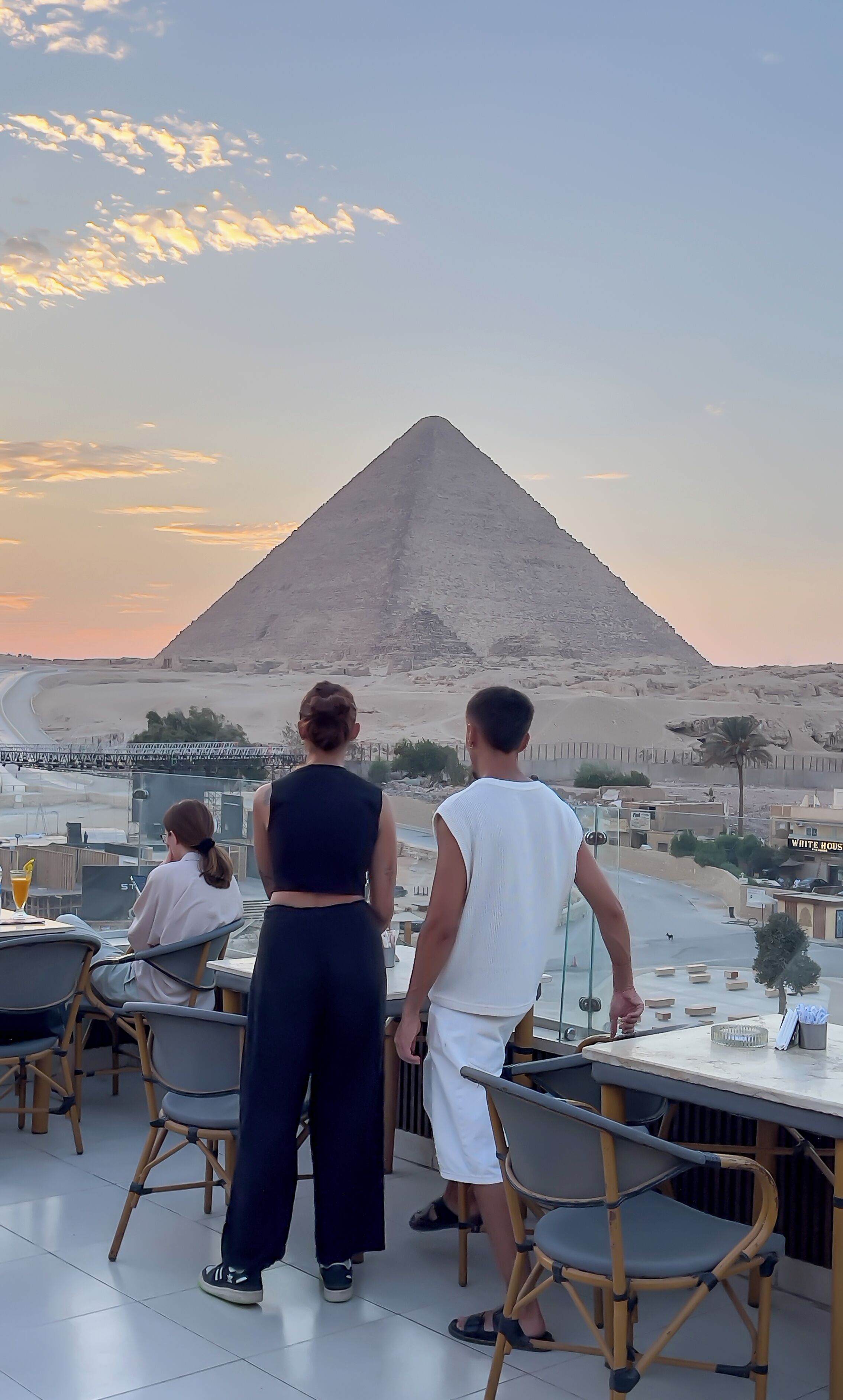 A terrace with a view of a pyramid, tables, and chairs.