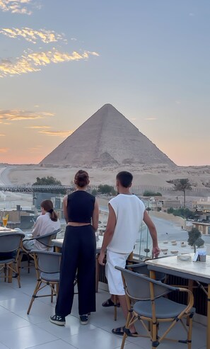 A terrace with a view of a pyramid, tables, and chairs.