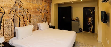 A hotel room with a large bed, a wall mural, a flat-screen TV, and a door leading to a bathroom.