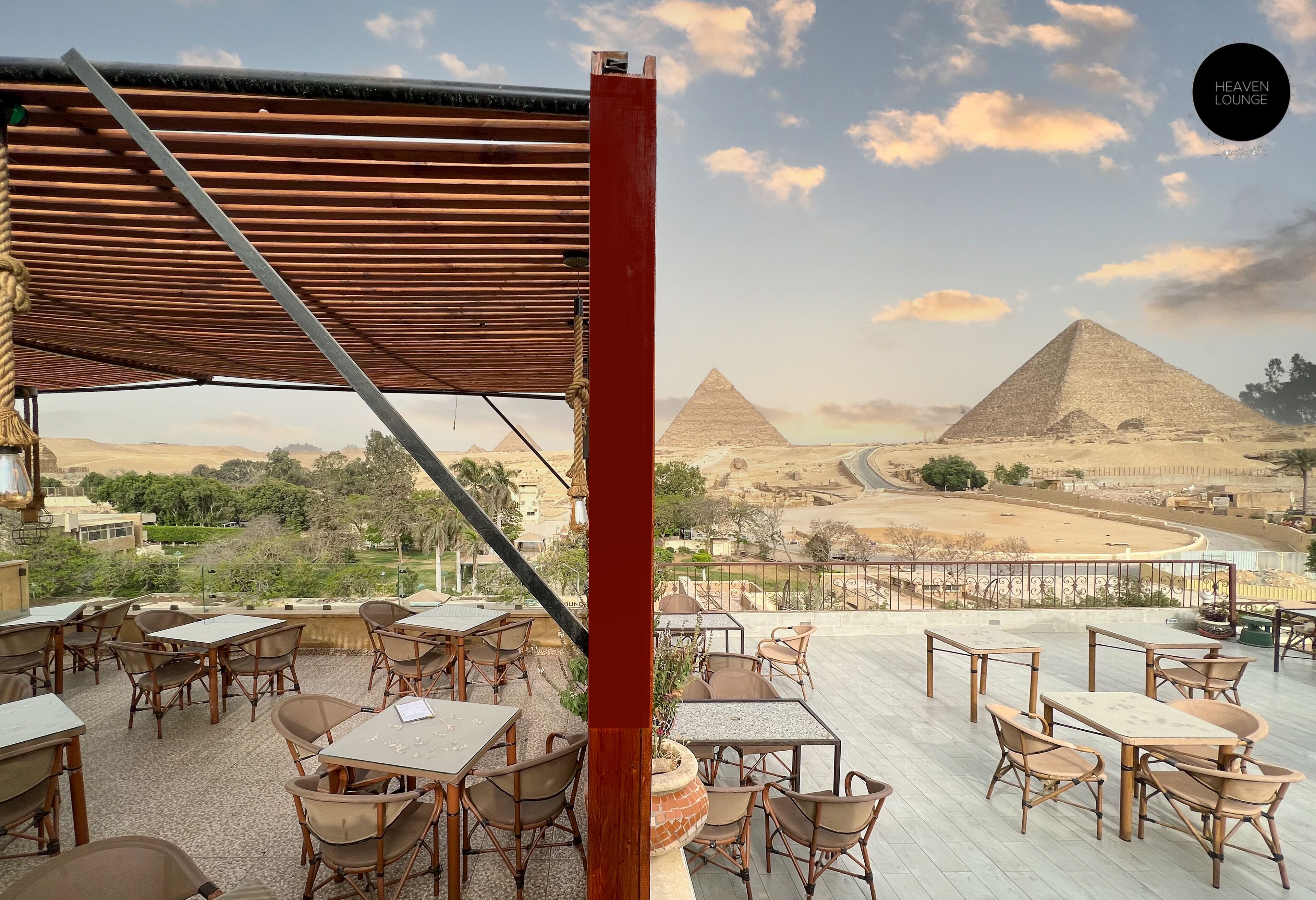 Un espace extérieur aménagé avec des tables et des chaises, offrant une vue sur un paysage désertique et des pyramides.