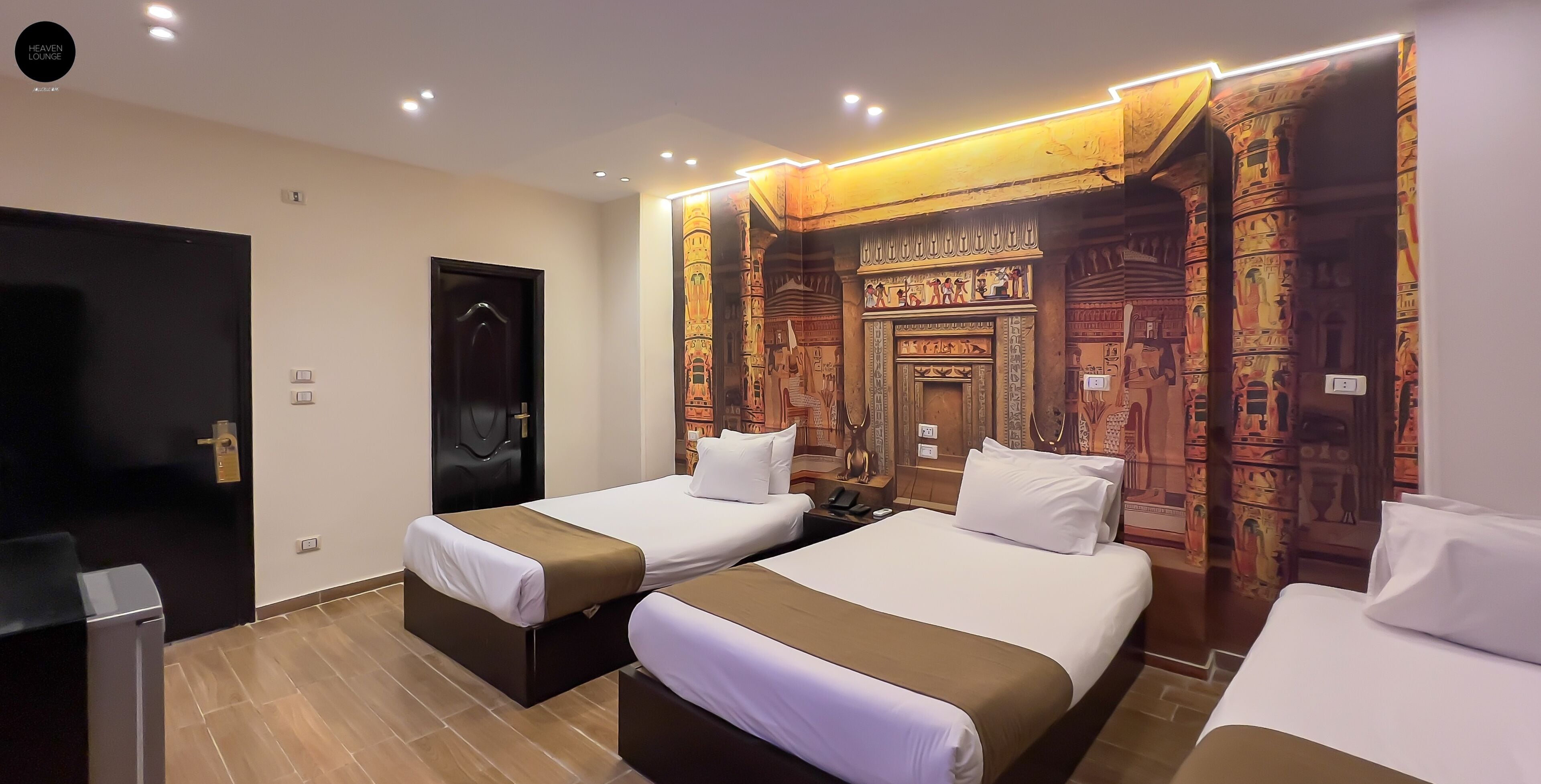 A hotel room with two beds, a black door, and Egyptian-themed wall art.