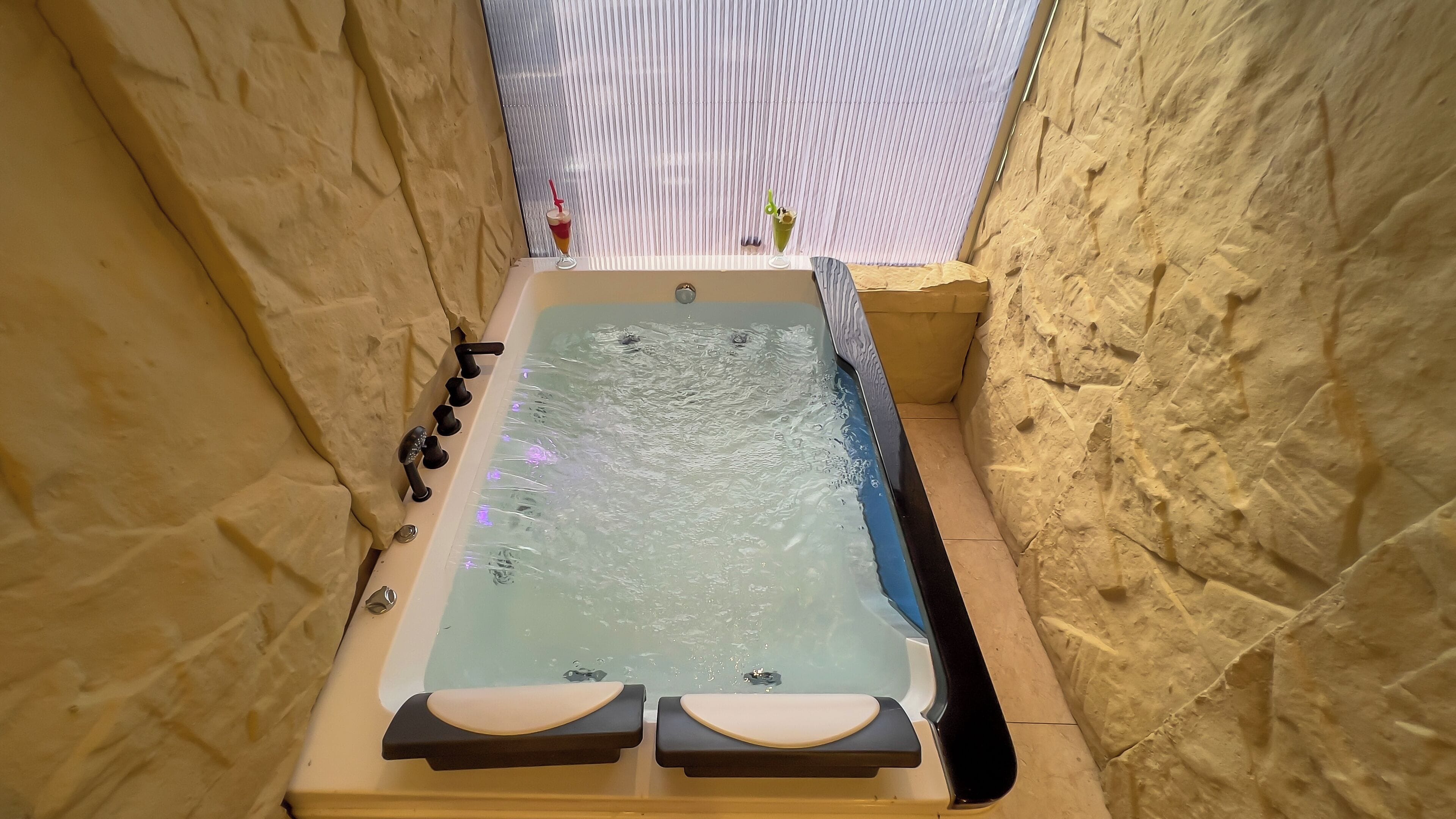 Ein Whirlpool vor einer Steinwand, ein Fenster mit Jalousien und ein Handtuchhalter.