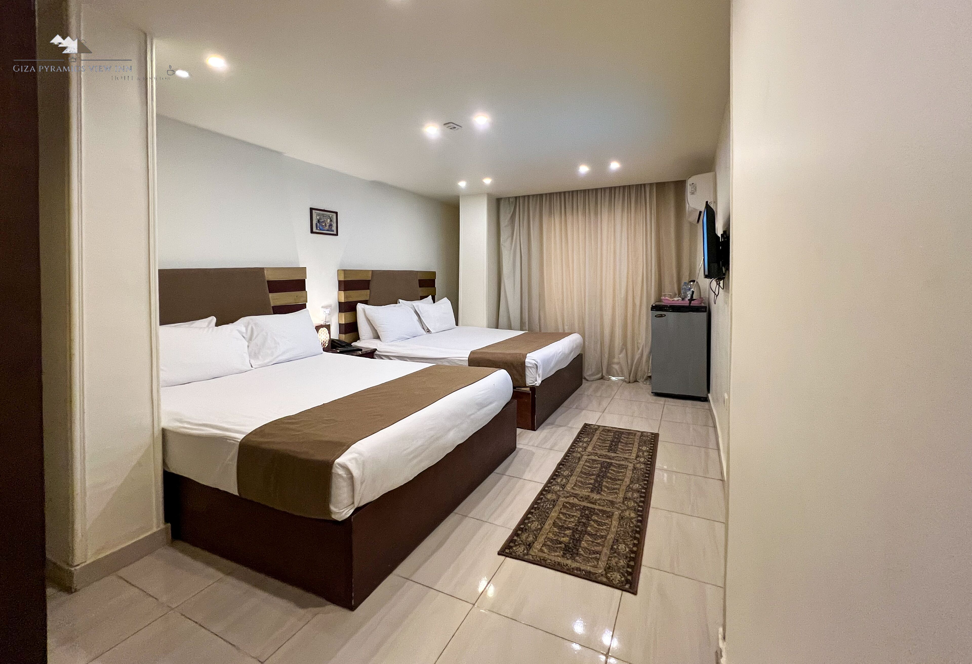 Une chambre d’hôtel avec deux lits, un bureau, une chaise, une télévision et une fenêtre avec des rideaux.