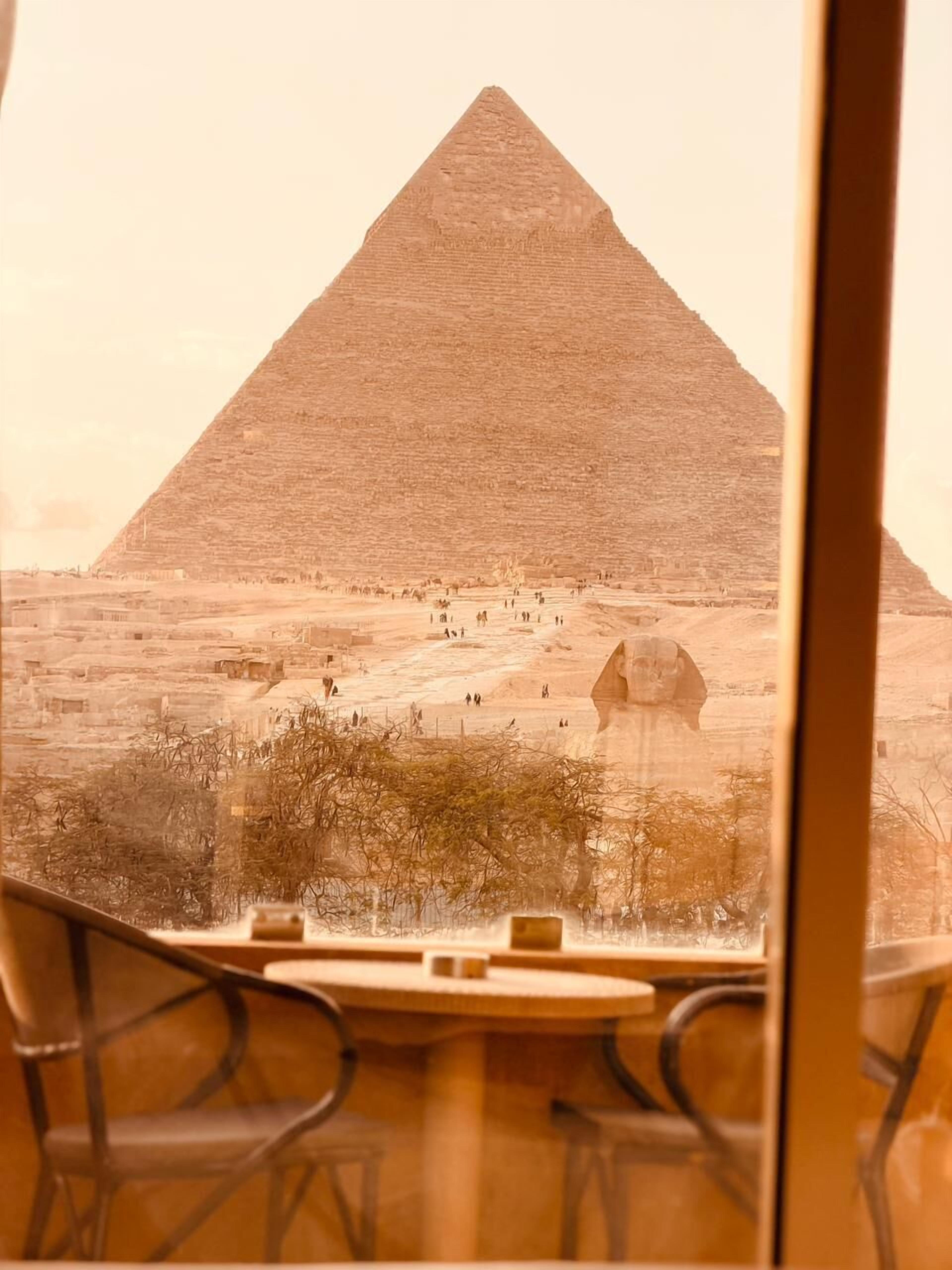 A view of the Great Pyramid of Giza from inside a building, with a table and chairs in the foreground.
