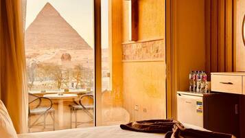 Une chambre d’hôtel avec vue sur la Grande Pyramide, un minibar et un coin repas avec des chaises.
