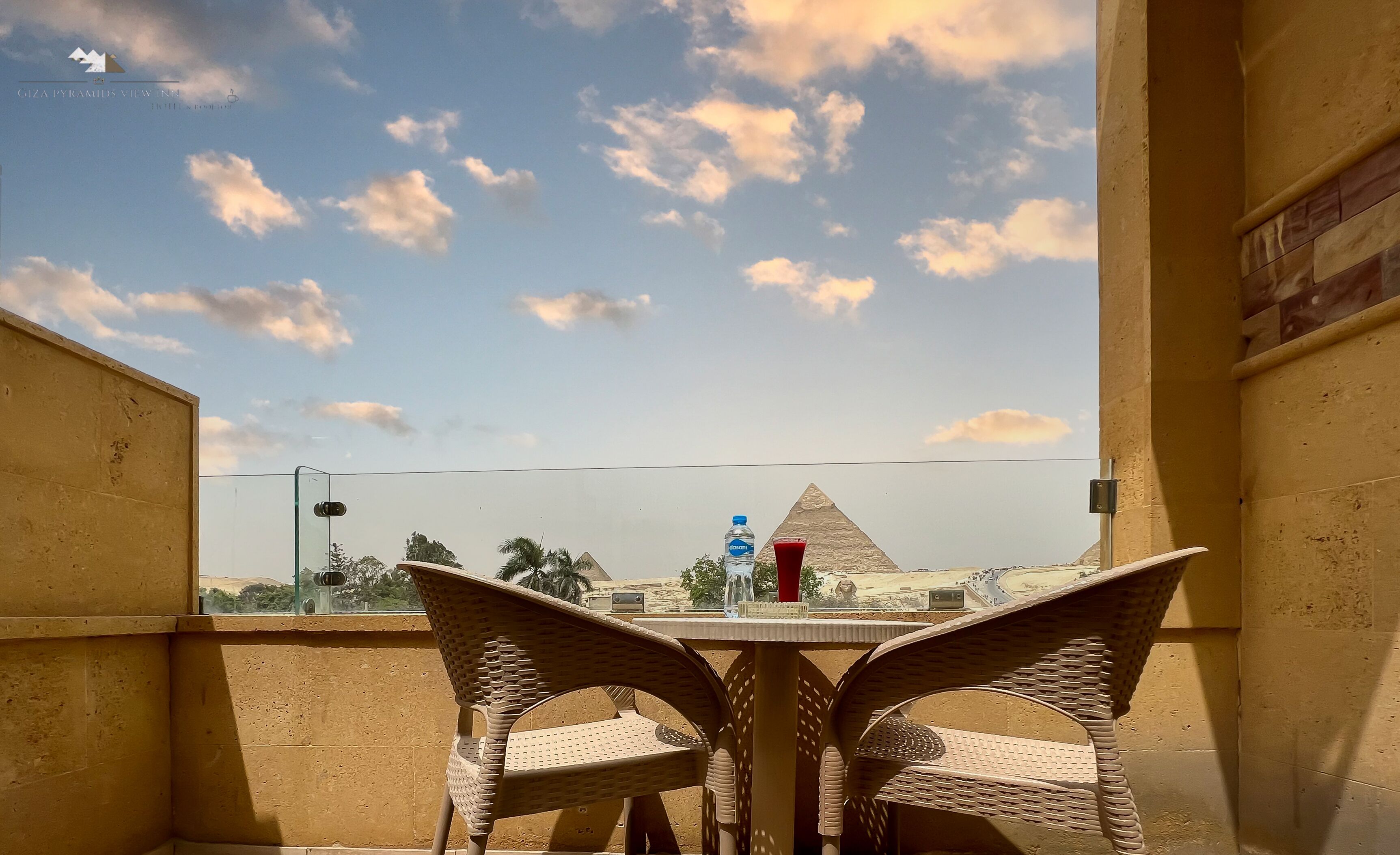 A balcony with wicker chairs, a table, and a view of pyramids in the distance.
