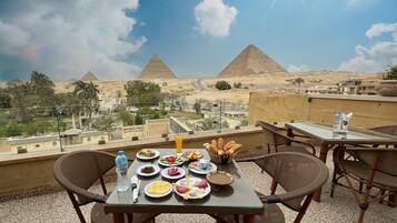 A table with food and drinks on a terrace overlooking pyramids.