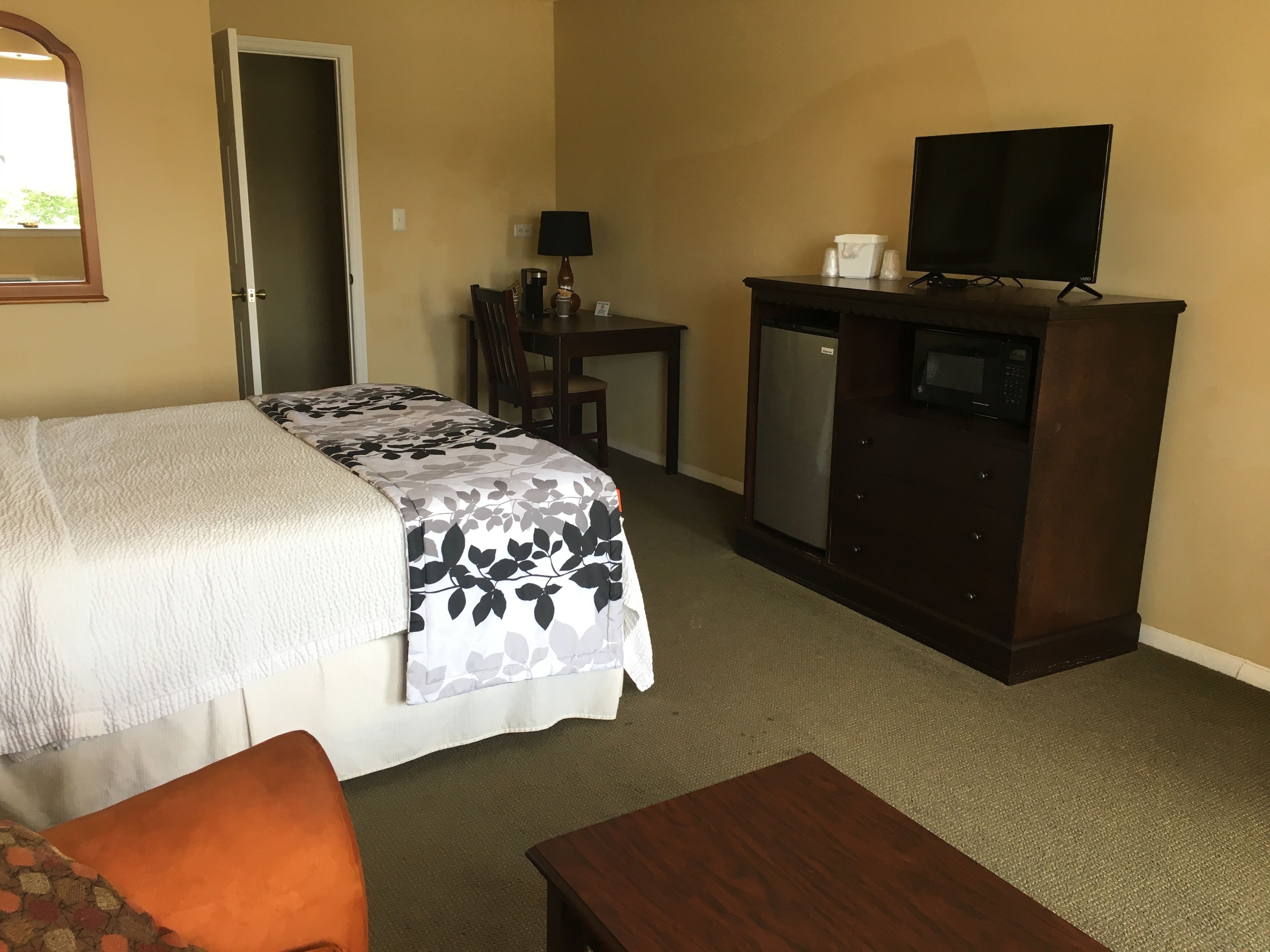 A hotel room with a bed, a desk, a television, and a refrigerator.
