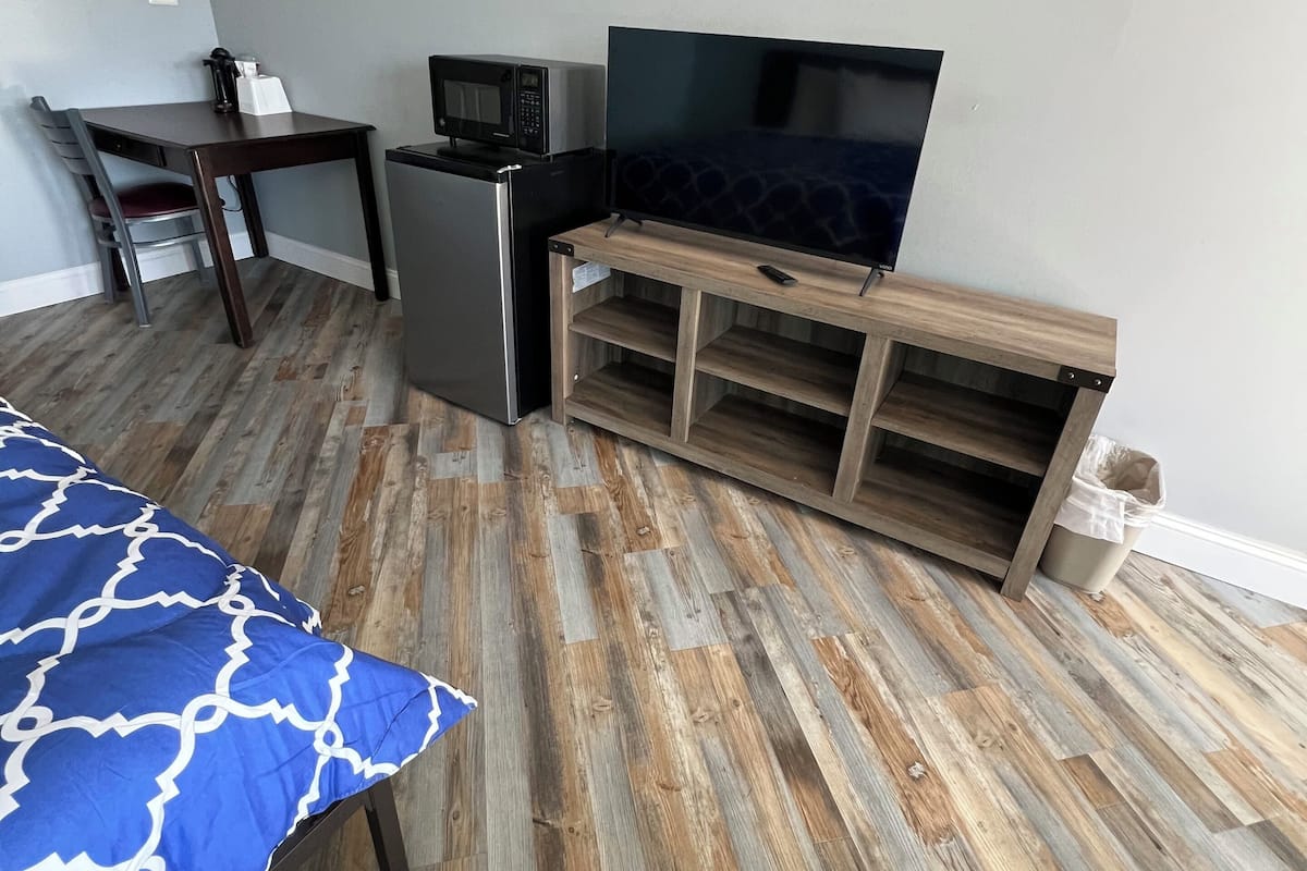 Une chambre avec un lit, un bureau, une télévision, un four à micro-ondes et une poubelle.