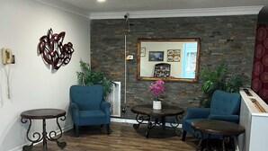 A lobby with two blue armchairs, a small round table, a decorative mirror, and a patterned rug. - Ambassador Inn And Suites (Manchester)