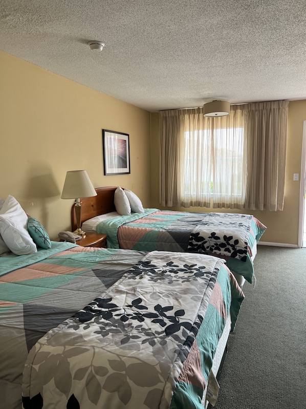 A hotel room with two beds, a nightstand, a lamp, a framed picture, and a window with curtains.