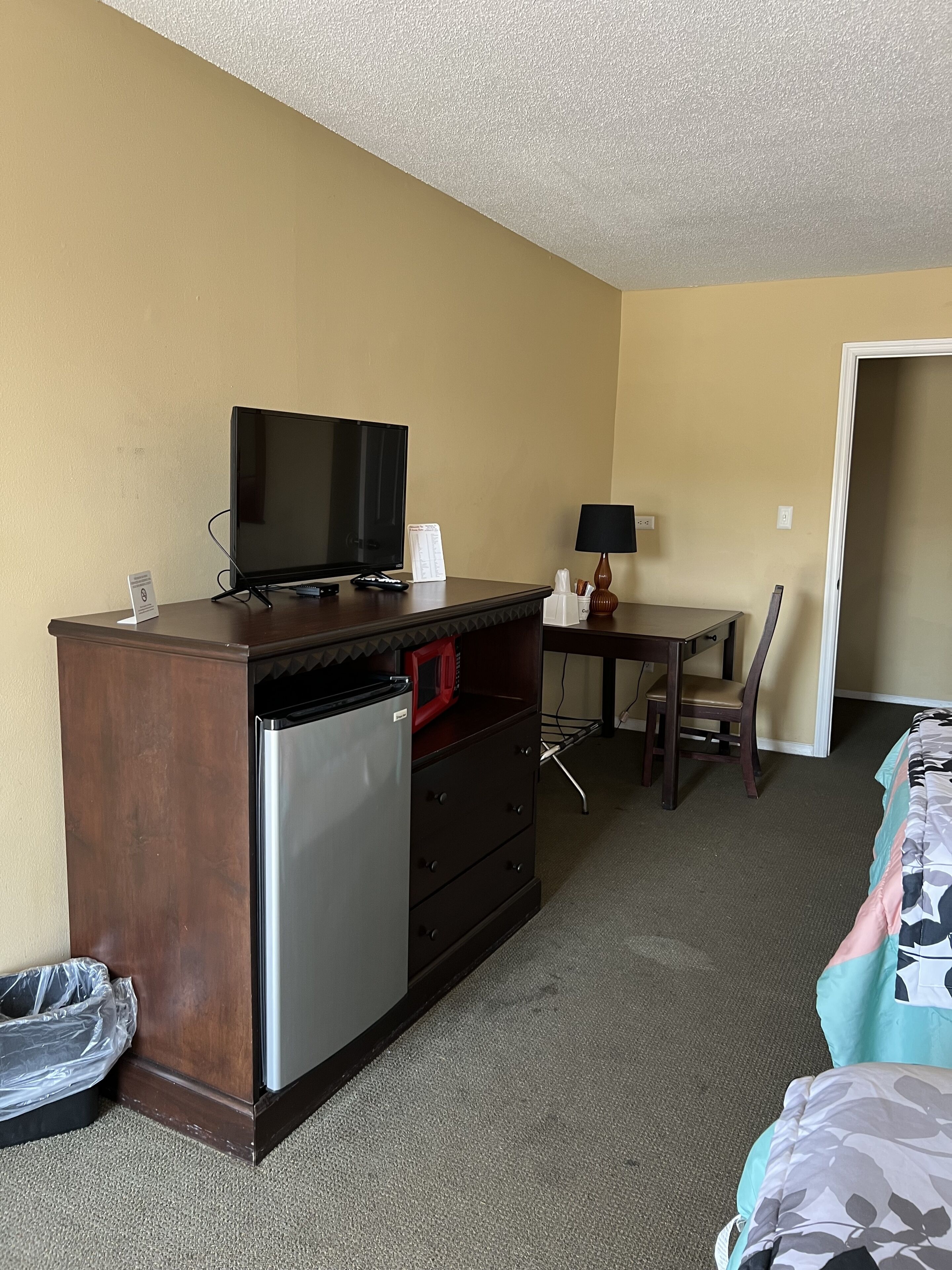 Hotelkamer met kitchenette, flatscreen televisie, magnetron, koelkast, bureau met stoel en bed met bloemenprint beddeken.