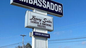 A sign for 'Ambassador' with 'Luxury Suites' and 'Exercise & Conference Facilities' below it, and a 'Senior Discount' sign at the bottom. - Ambassador Inn And Suites (Manchester)