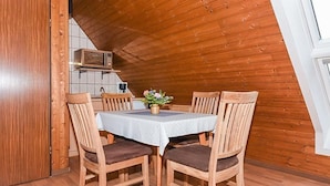 Un coin repas avec une table dressée pour quatre personnes, des chaises en bois, une petite plante en pot et un four à micro-ondes placé au-dessus du comptoir.