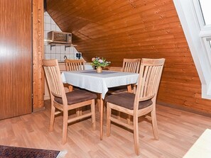 A dining area with a table set for four, wooden chairs, a small potted plant, and a microwave above the counter.