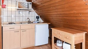 Une cuisine compacte aux murs en bois, équipée d’un four à micro-ondes, d’un évier, d’un réfrigérateur et d’une petite table en bois.