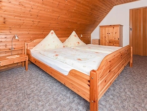 A wooden bed in a room with a sloped ceiling and a wardrobe.