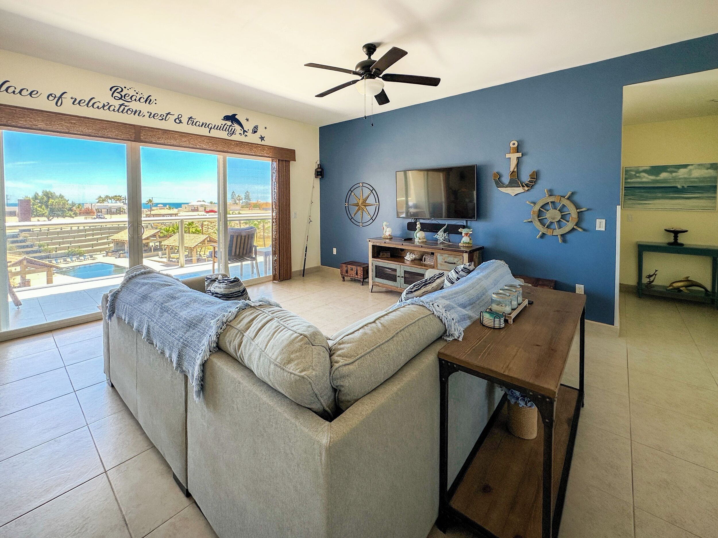 A living room with a large window, a ceiling fan, a TV, and nautical-themed decor.