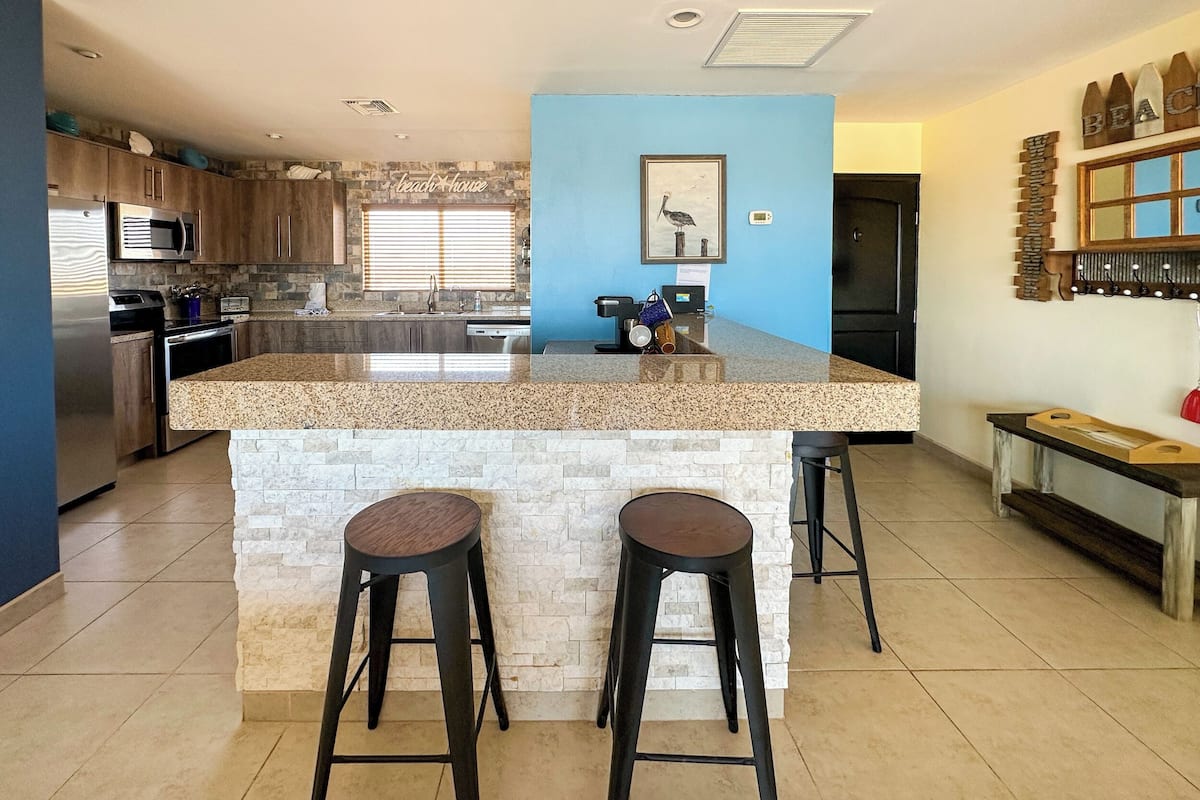 Una cocina moderna con encimeras de granito, dos taburetes de bar, una isla integrada y una pared azul de acento.