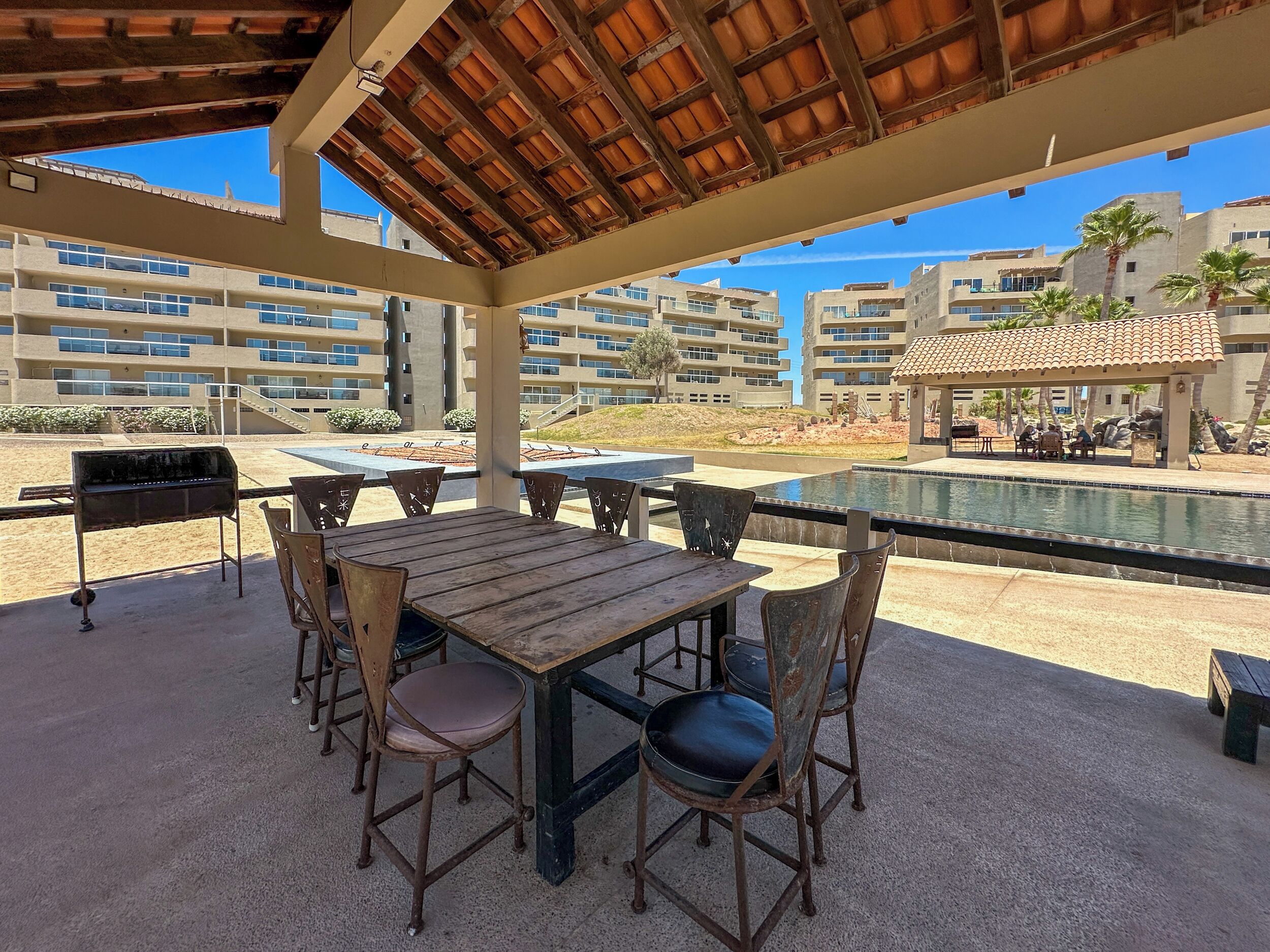 Une terrasse extérieure avec une table et des chaises en bois, un barbecue et une piscine.