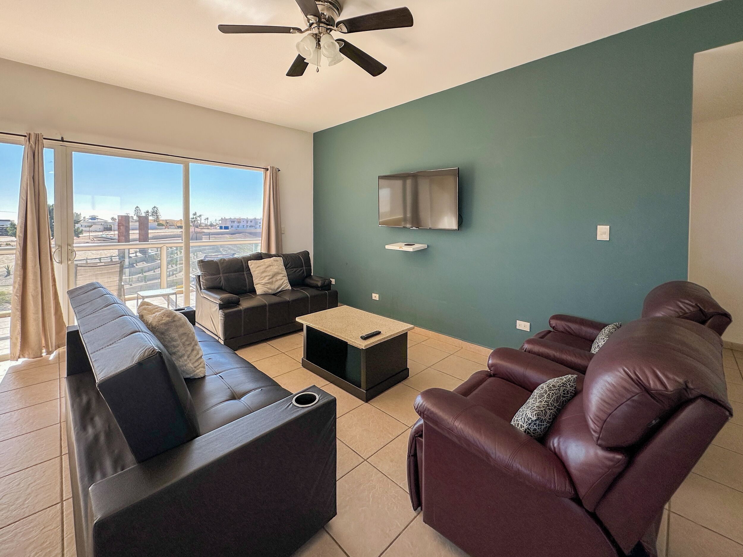 Un salon moderne avec un canapé, un fauteuil inclinable et une table basse. Un téléviseur est fixé au mur et un ventilateur de plafond est installé au plafond.