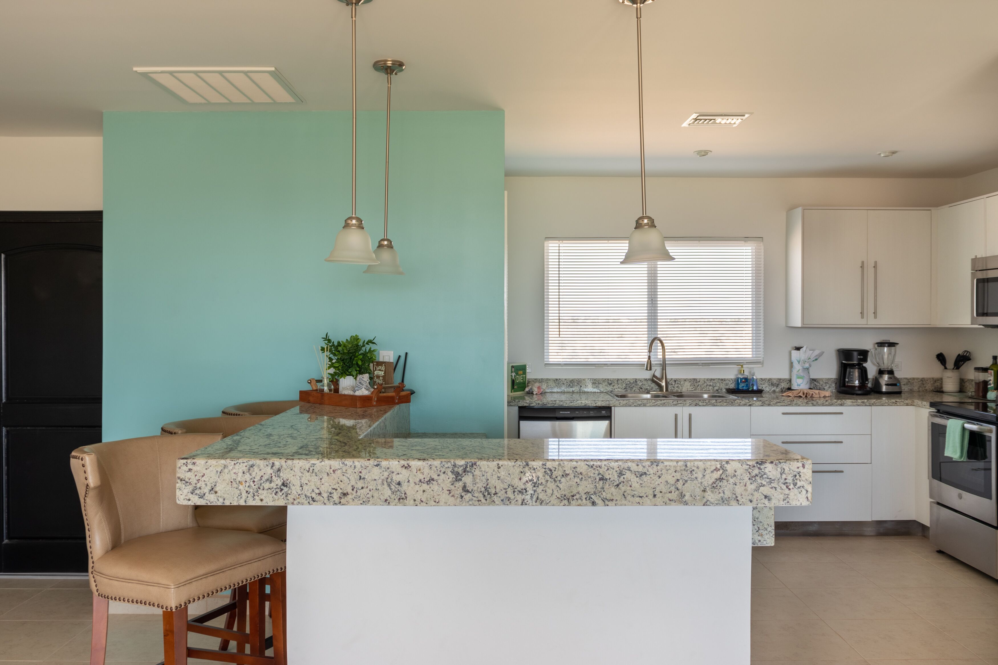 Een keuken met een centraal eiland, witte kasten, een zwarte koelkast en hanglampen.