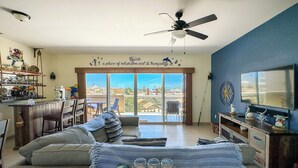A living room with a sofa, a coffee table with jars, a TV, and a balcony with a view.