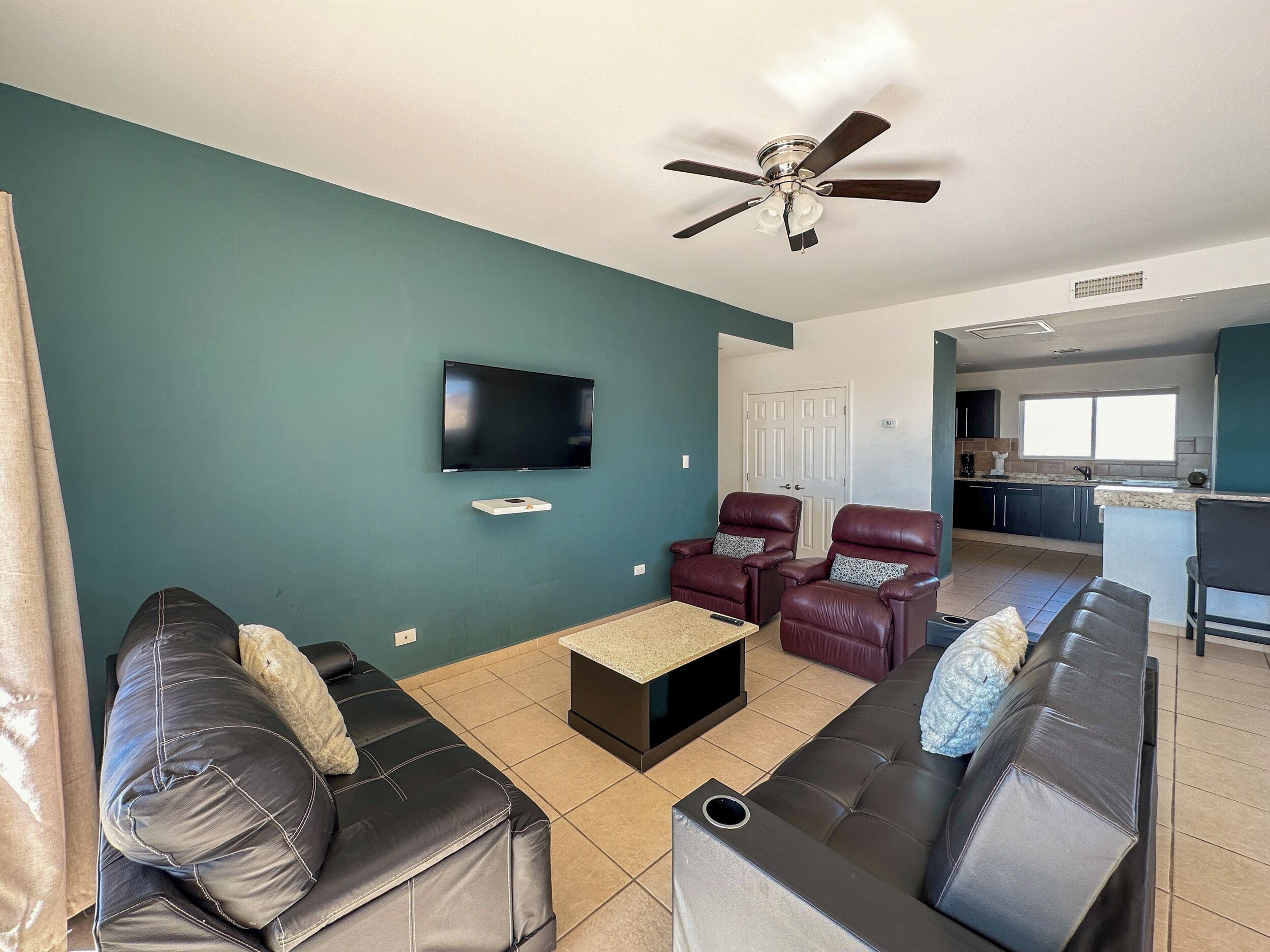A living room with a TV, two leather sofas, a coffee table, and a ceiling fan.