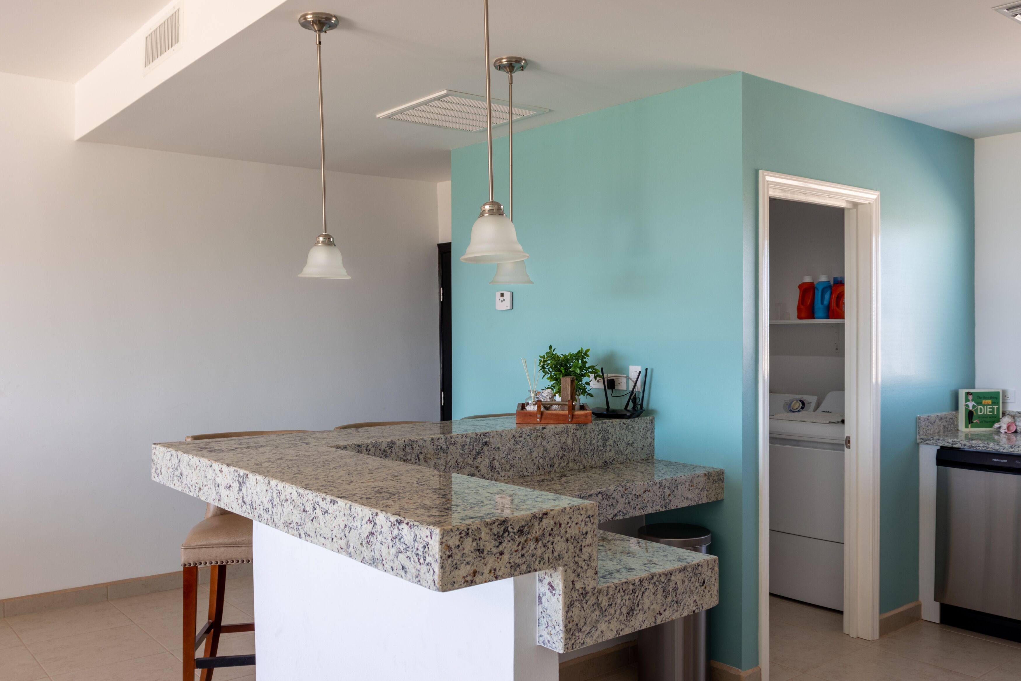 A kitchen with a granite countertop, a hanging light fixture, and a view into the adjacent laundry room.