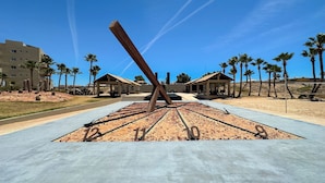 A desert landscape with a large metal sculpture, palm trees, and a building in the background.