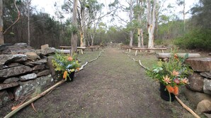 A pathway flanked by stone walls and wooden benches, leading through a forested area. - Hobart Bush Cabins (Kingston)