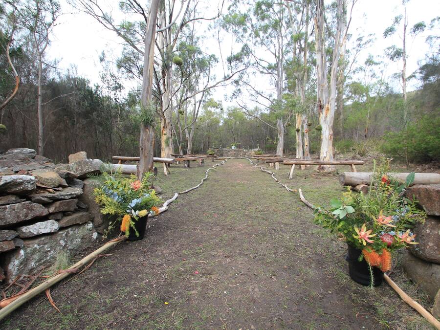 A pathway flanked by stone walls and wooden benches, leading through a forested area.