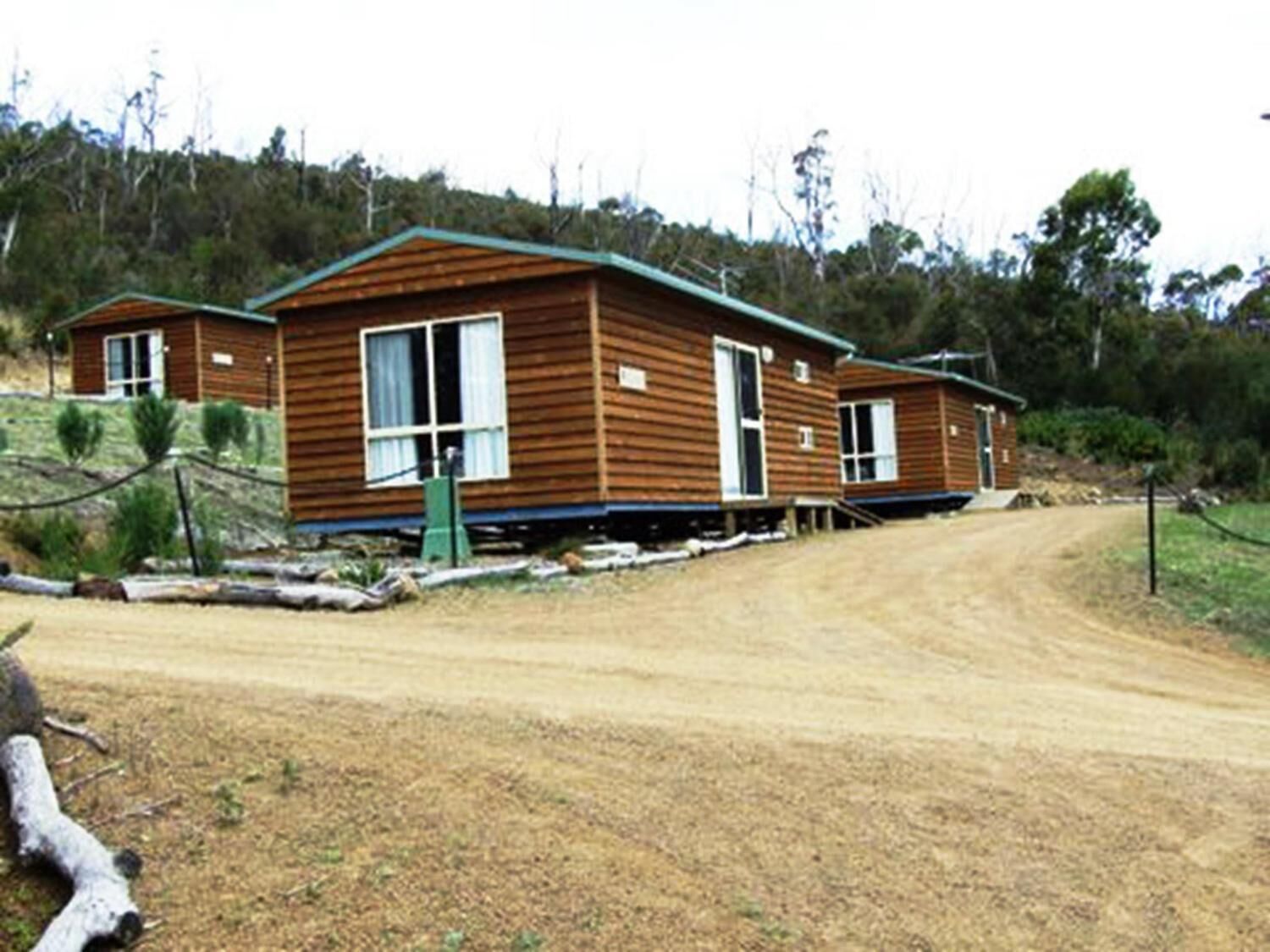 A wooden cabin with a dirt road leading to it, surrounded by trees.