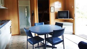 A compact kitchen with a round table and chairs, a television on a shelf, and a door leading to an outdoor area. - Hobart Bush Cabins (Kingston)