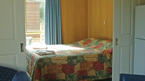 A bedroom with a bed, a window with curtains, and a door. - Hobart Bush Cabins (Kingston)