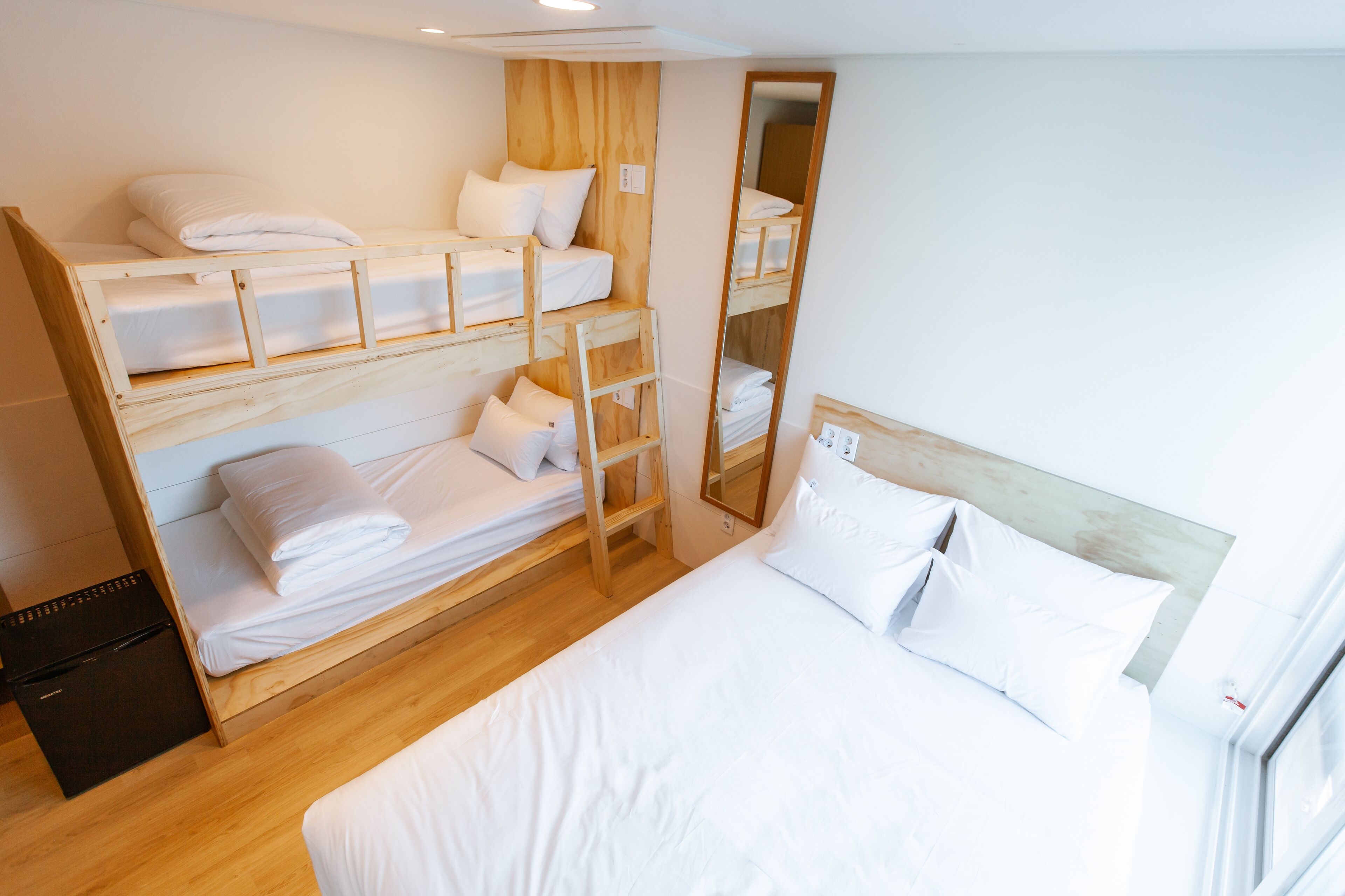 A bunk bed room with a wooden ladder, a large mirror, and a single bed with white bedding.