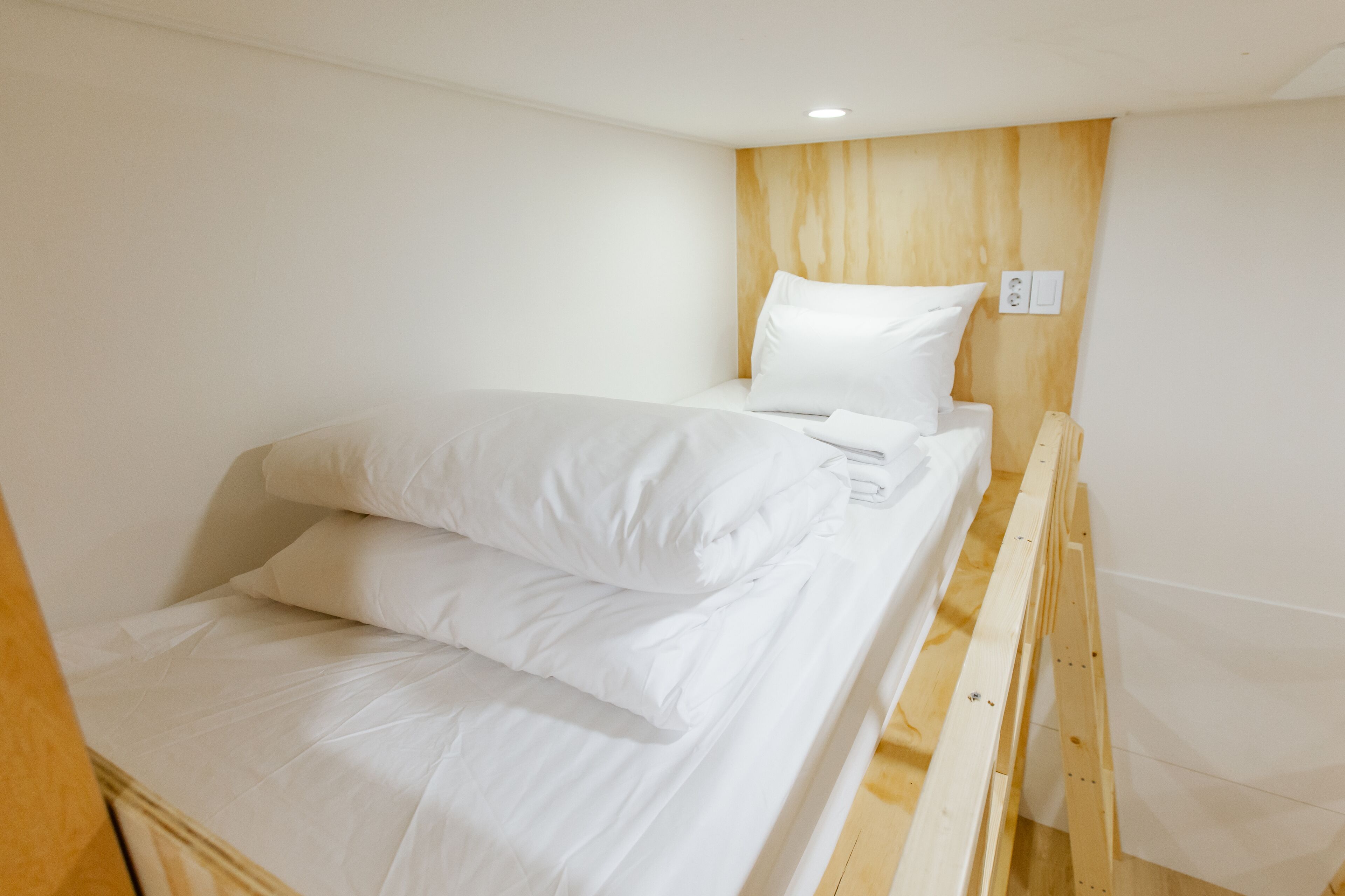 A single bed with white bedding in a room with a wooden headboard and white walls.