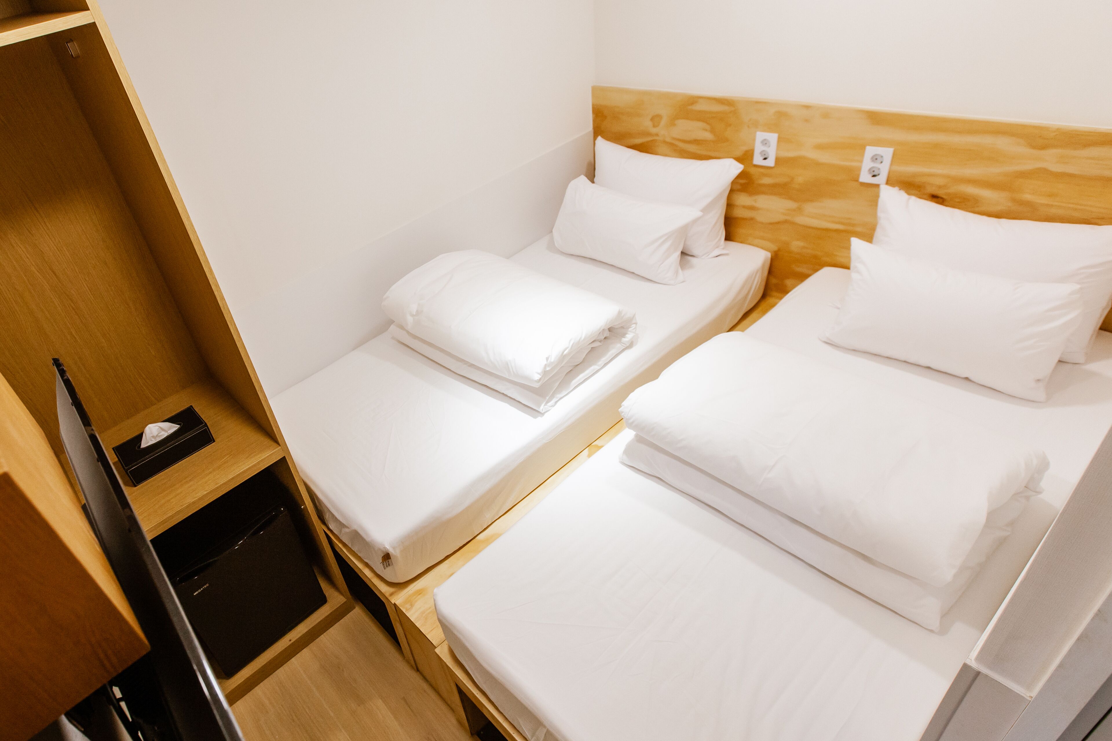 Habitación de hotel con dos camas individuales, cabeceros de madera y un pequeño mueble de madera con una caja de pañuelos.