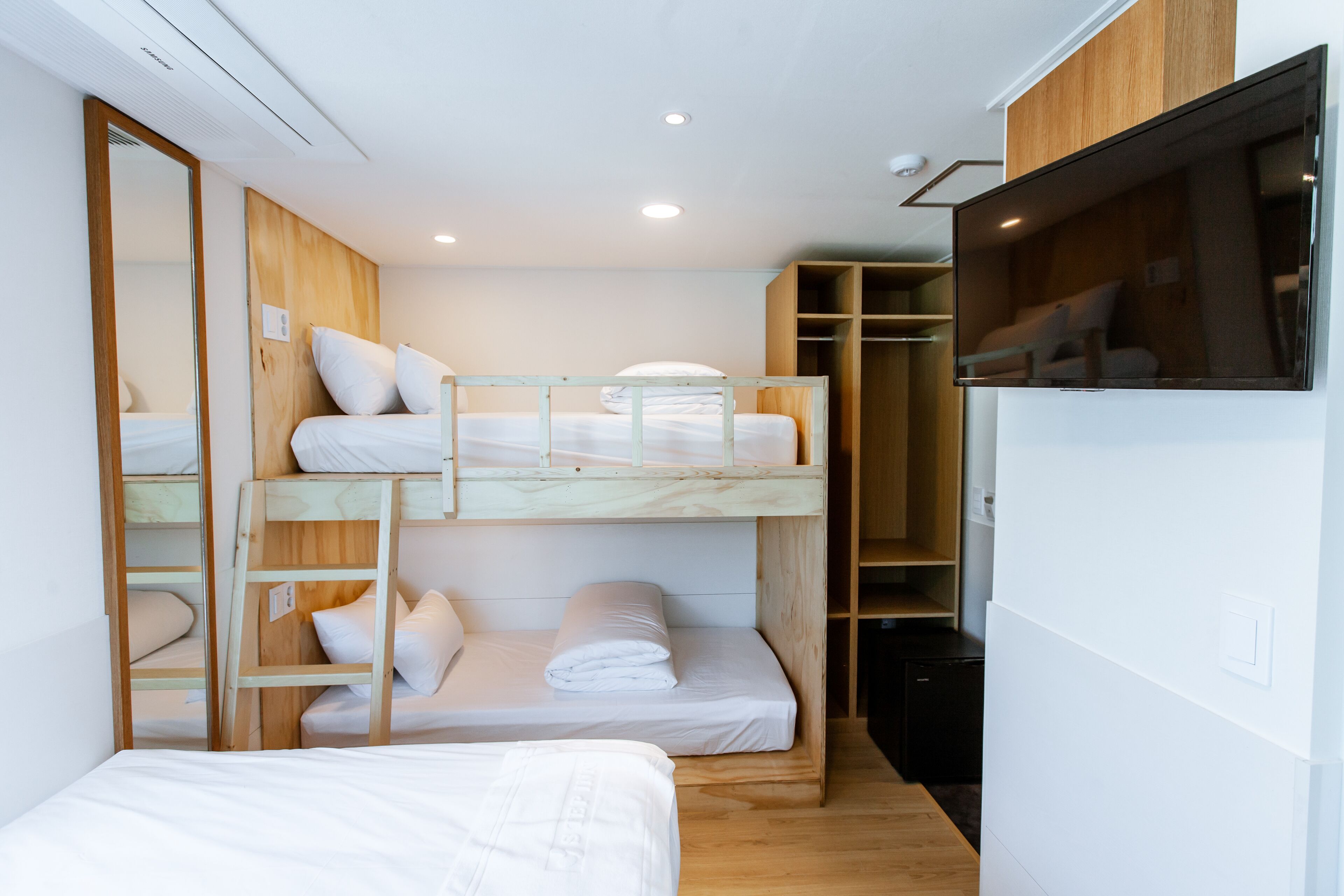 A compact, modern room with bunk beds, a wardrobe, and a television.
