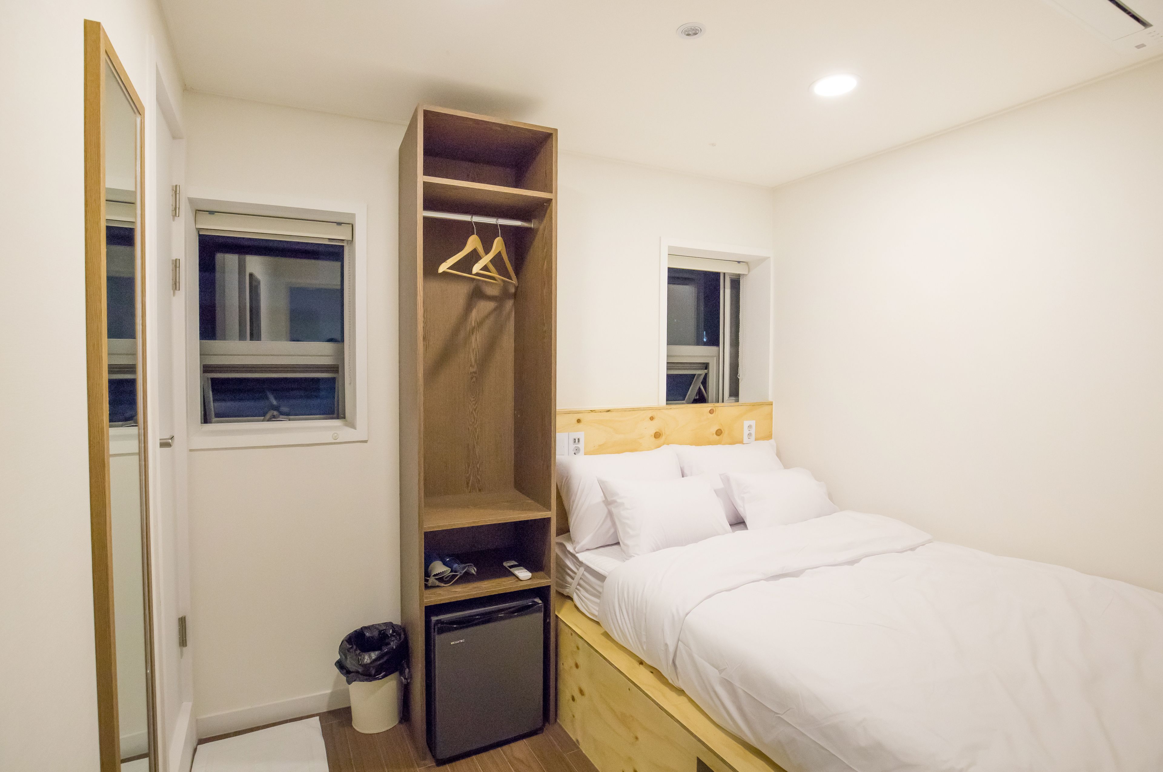 A bedroom with a bed, a wardrobe, a small fridge, and a window.