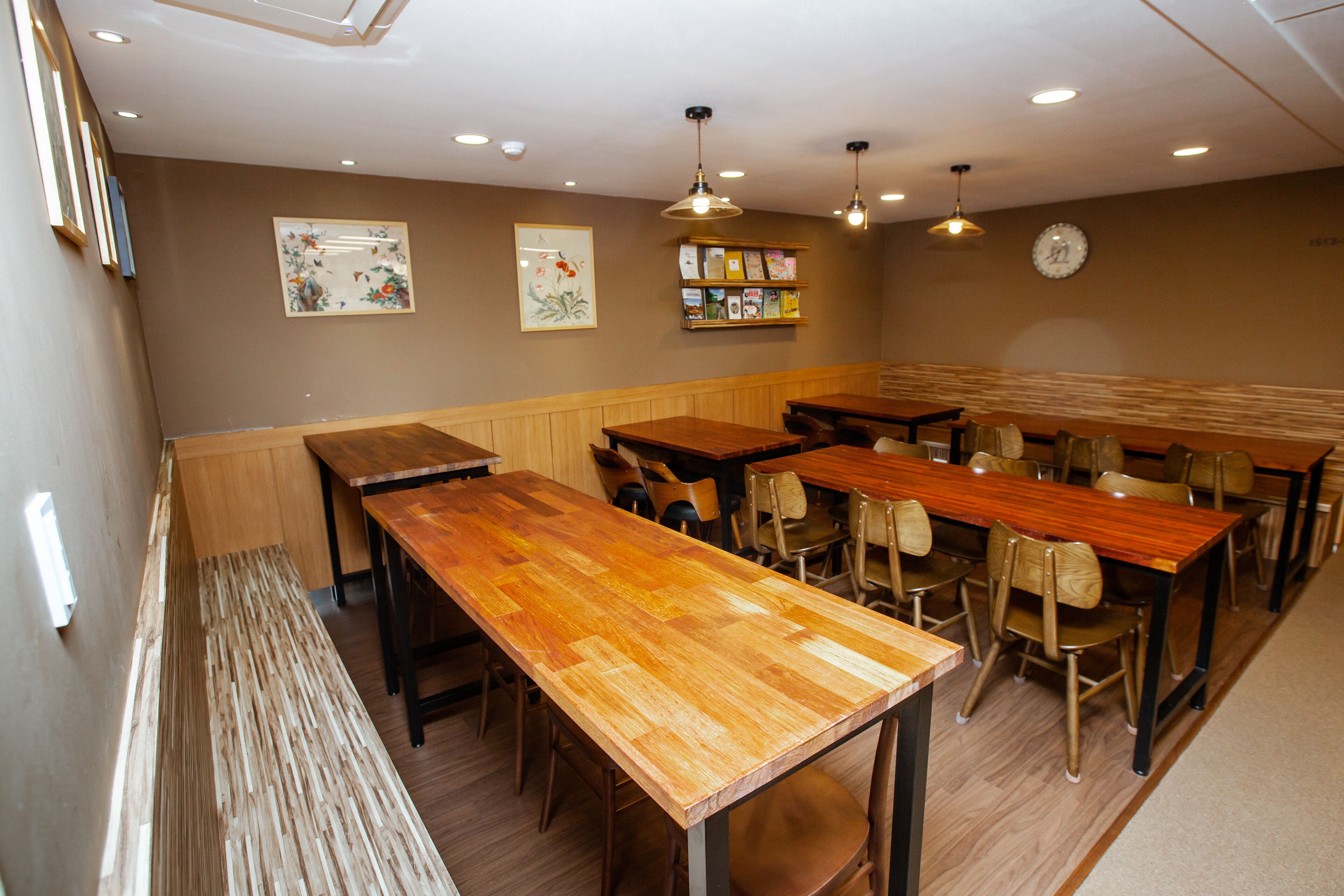 A restaurant with wooden tables and chairs, a clock on the wall, and framed artwork.