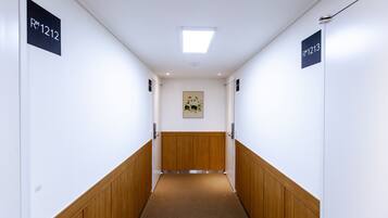 Ein Flur mit Holzwandverkleidung und Teppichboden, der von weißen Wänden mit Raumschildern RM1212 und RM1213 gesäumt wird.